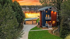 A modern two-story house with a garage, a covered driveway, and a view of a lake at sunset. - Blue Haven (Mooresville)