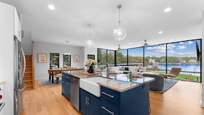 A modern kitchen with a large island, wooden flooring, and a view of a lake. - Blue Haven (Mooresville)