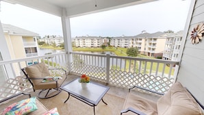 A balcony with a view of a residential area, a table with a vase of flowers, and two chairs. - Magnolia Pointe Luster Leaf 4895-402 (Myrtle Beach)