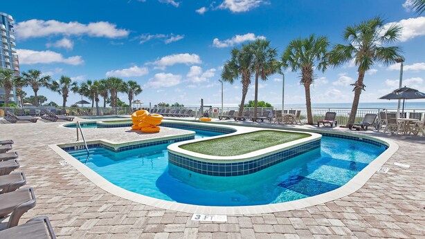 A swimming pool with multiple lanes, lounge chairs, and palm trees. - Atlantica 903 (Myrtle Beach)