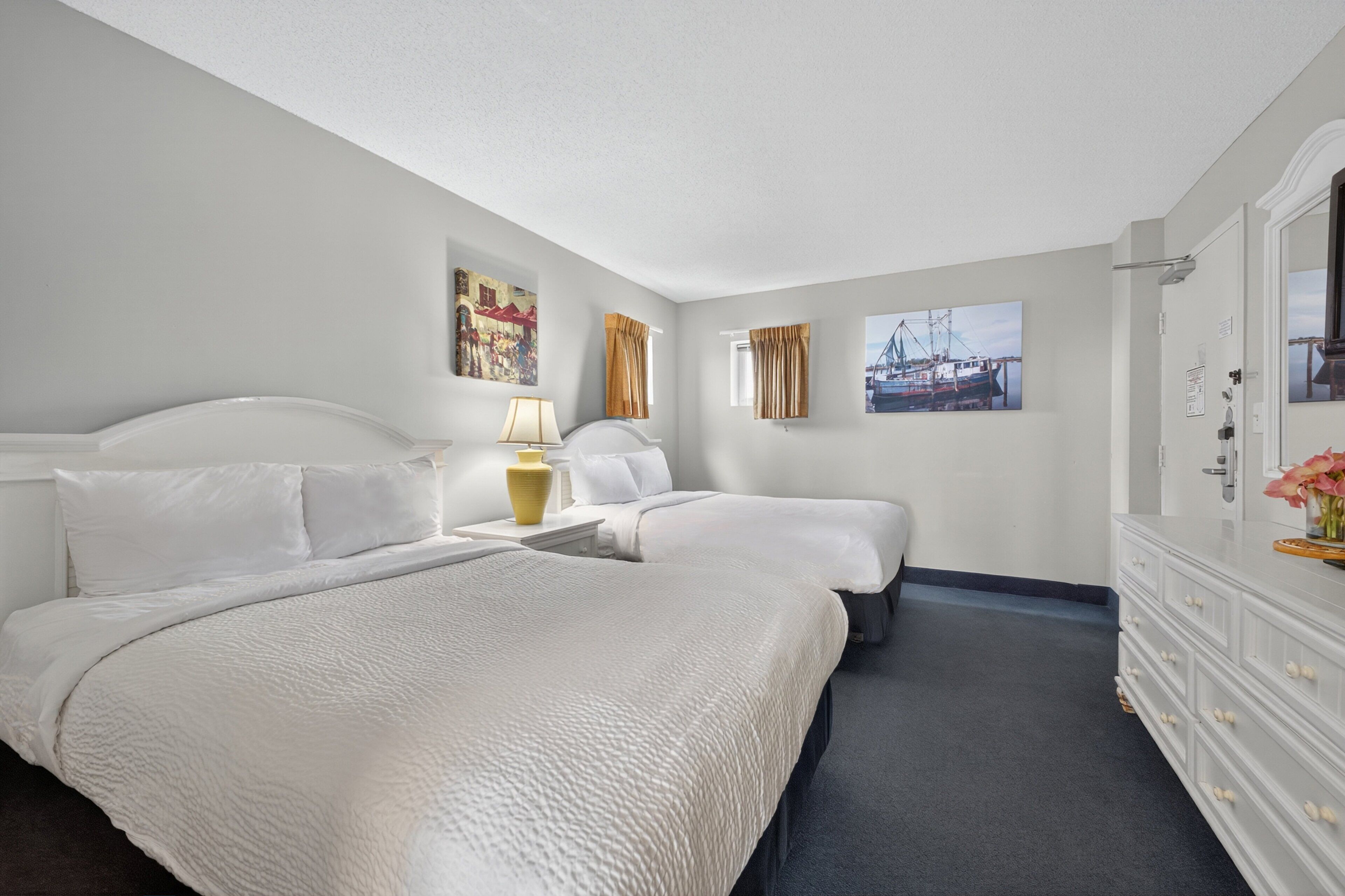 Ein Hotelzimmer mit zwei Betten, einem Nachttisch mit Lampe, einem Schminktisch und Bildern an den Wänden.