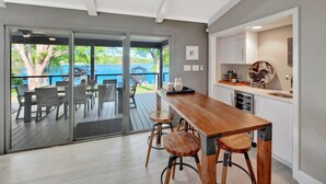 A modern kitchen with a wooden table and bar stools, a sliding glass door leading to a deck, and a view of a lake. - Southern Sunrise (Mooresville)