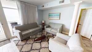 Ein Wohnzimmer mit einer Couch, einem Sessel und einem Couchtisch. An der Wand hängt ein Gemälde, und rechts ist eine Tür zu sehen.