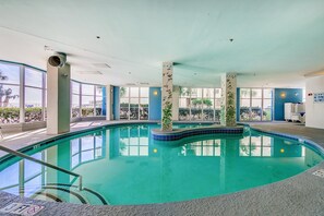 Ein Hallenbad mit großen Glaswänden, gefliestem Boden und einem Rettungsschwimmerstand.