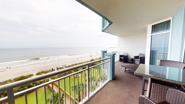 Ein Balkon mit Blick auf den Strand, einem Tisch und zwei Stühlen.