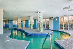 Ein Hallenbad mit klarem, blauem Wasser, umgeben von blauen Wänden und Säulen mit grünen Pflanzenmustern.