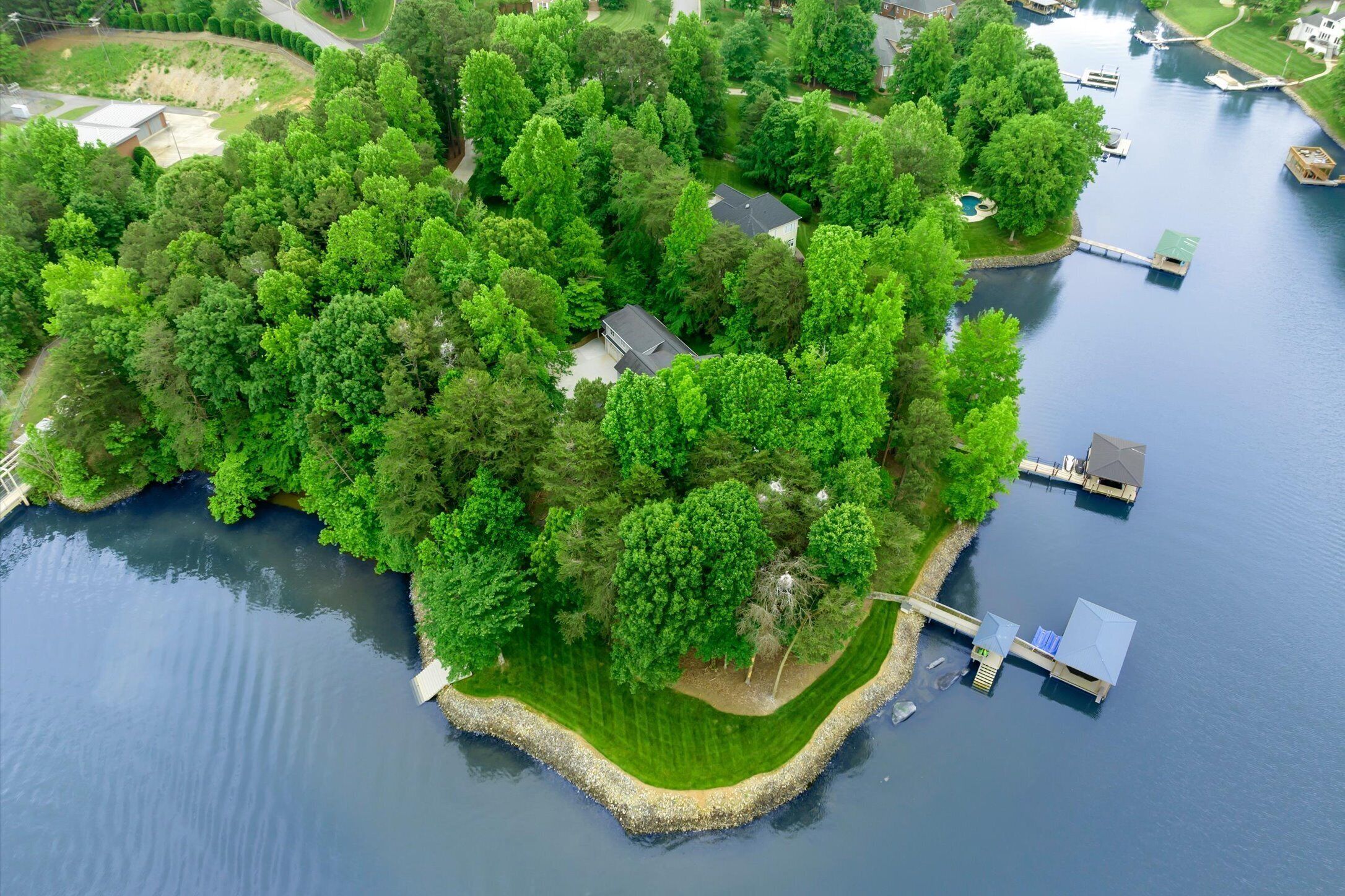 Eine Vogelperspektive einer abgelegenen Insel mit dichter Vegetation, einem kleinen Haus und Anlegestellen, die sich in ruhiges Gewässer erstrecken.