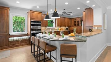 A kitchen with wooden cabinets, a central island with bar stools, pendant lighting, and a ceiling fan.