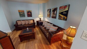 Ein Wohnzimmer mit zwei Ledersofas, einem Couchtisch und einer Lampe. An den Wänden hängen Poster.