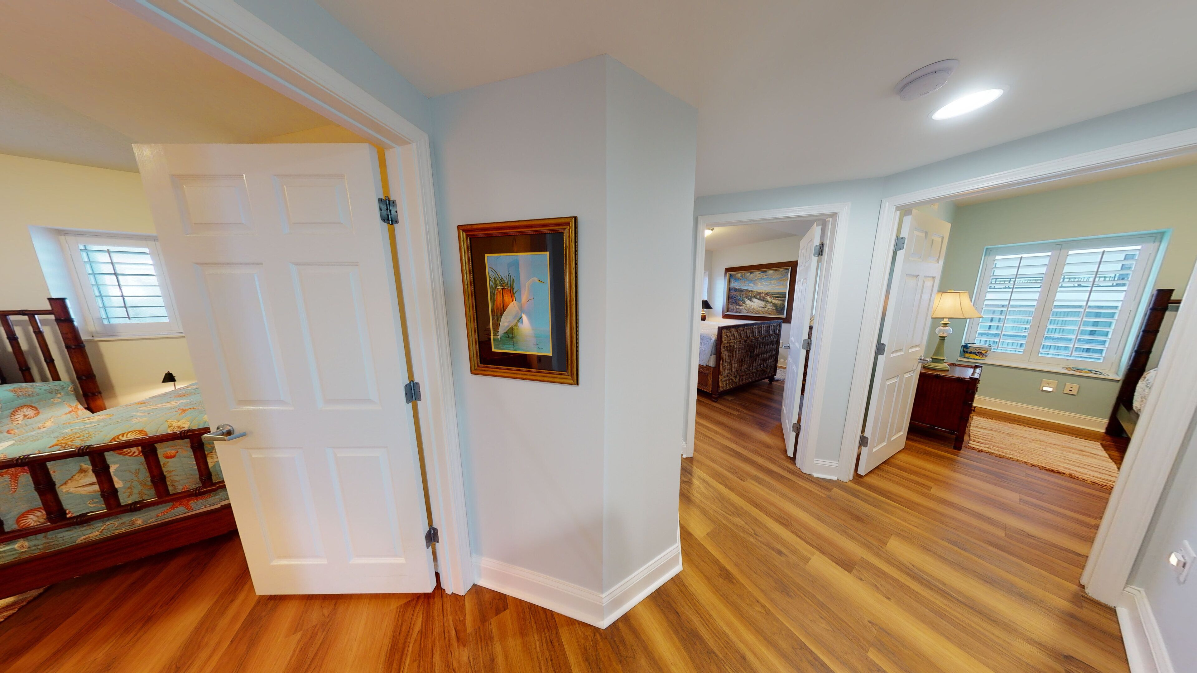 A spacious room with hardwood floors, a bed with a floral bedspread, a painting on the wall, and a view of the outside through a window.