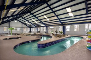 Una piscina interior con varias pistas de natación, techo cubierto y zona de estar con sillas.