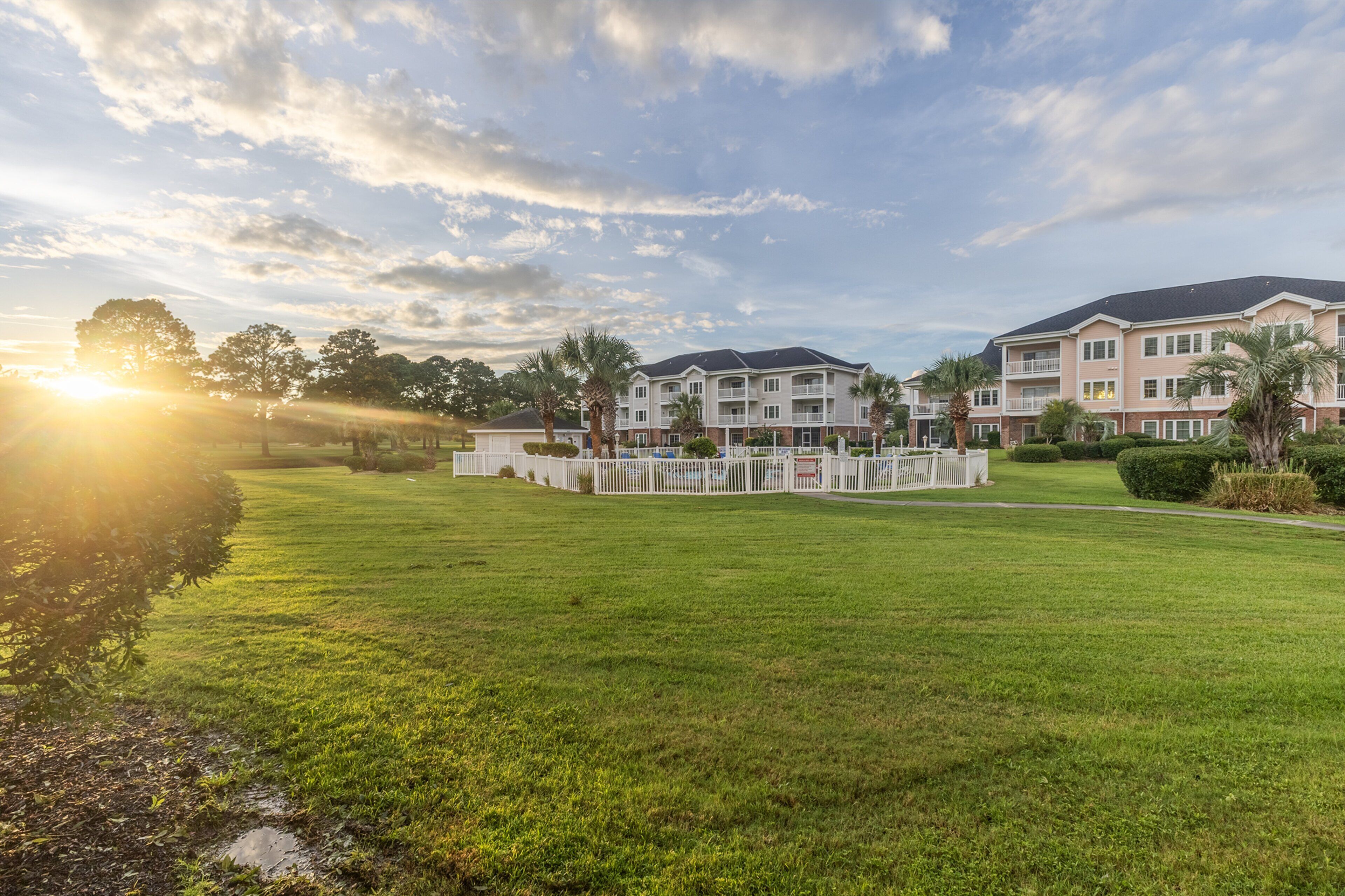 A multi-story hotel with a well-maintained lawn and a white fence surrounding the property.
