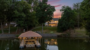 A lakeside property with a dock, a covered seating area, and a large house with a well-maintained lawn. - Waddell Waters (Mooresville)