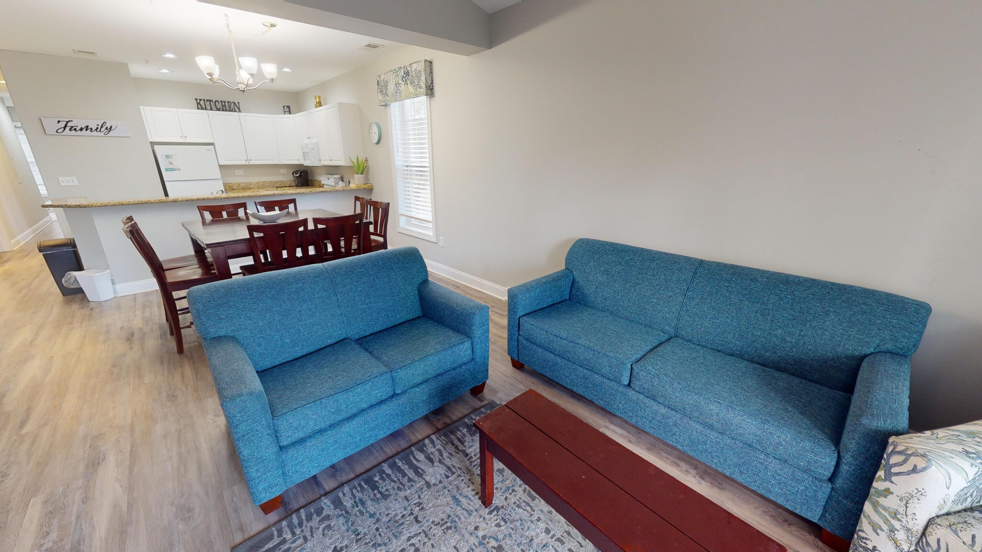 A living room with two blue sofas, a wooden coffee table, and a dining area with wooden chairs and a table.