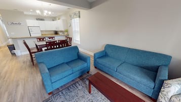 A living room with two blue sofas, a wooden coffee table, and a dining area with wooden chairs and a table.