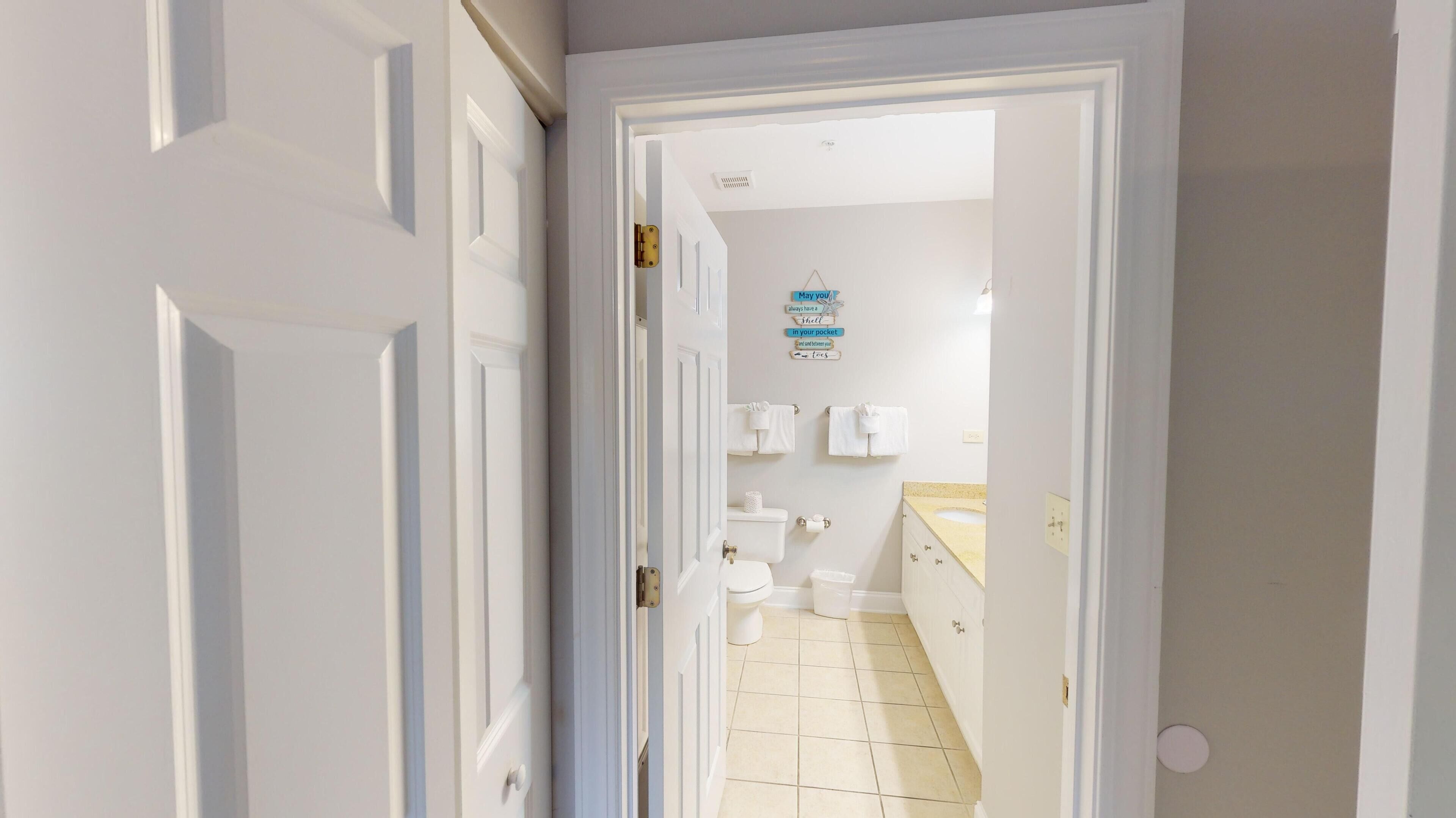 A narrow hallway leading to a bathroom with a toilet, sink, and towel rack.