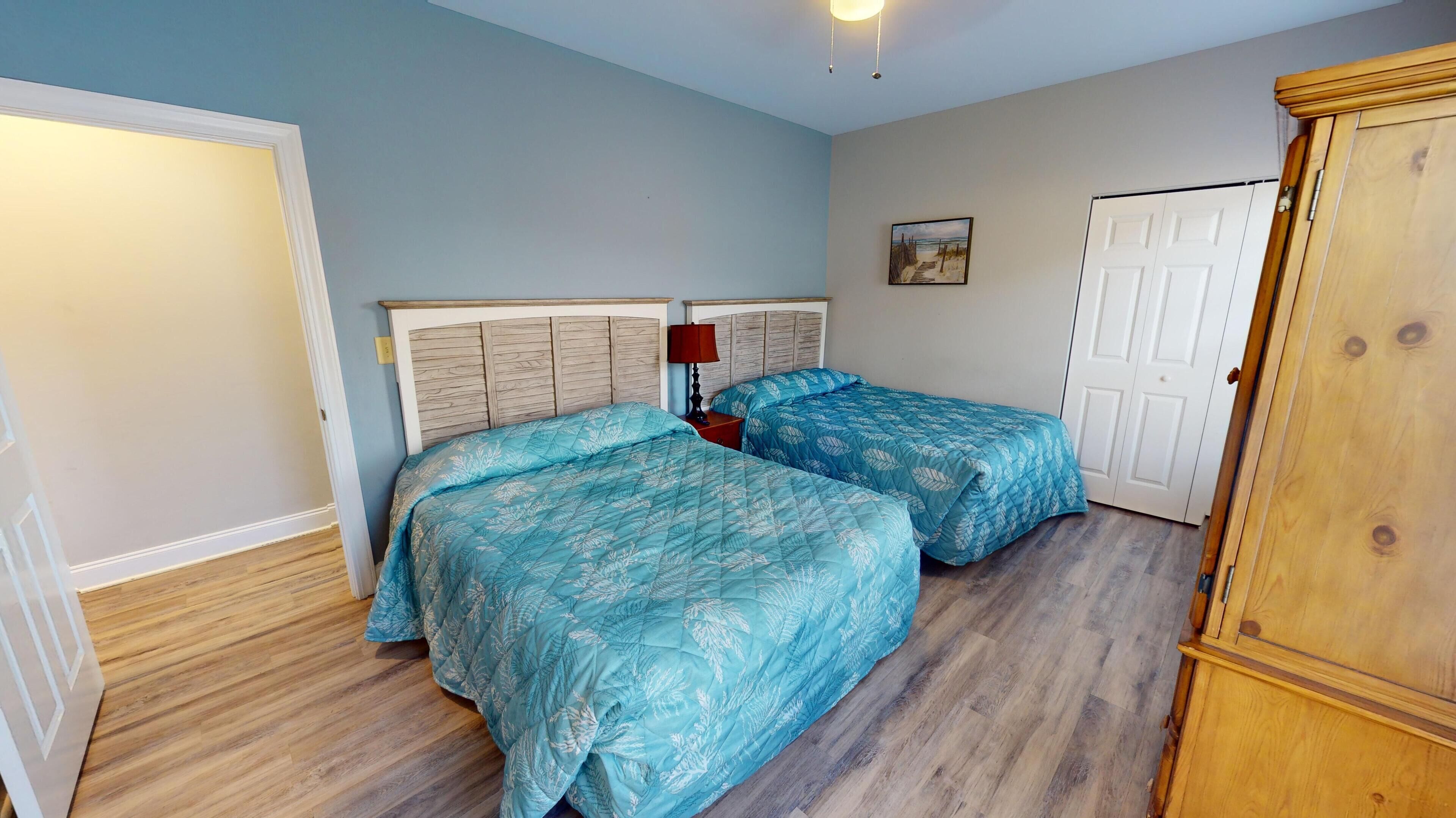 A bedroom with two beds, a wooden wardrobe, and a painting on the wall.