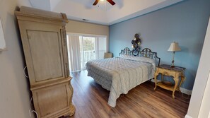 Une chambre dotée d’une grande armoire en bois, d’un lit recouvert d’une courtepointe matelassée, d’une table de chevet avec une lampe, et offrant une vue sur l’extérieur grâce à une porte-fenêtre coulissante.