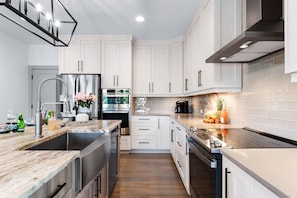A modern kitchen with white cabinets, stainless steel appliances, and a marble countertop. - Elysian Shores (Mooresville)