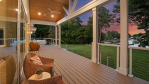 A covered outdoor deck with wicker furniture, a ceiling fan, and a view of a lake at sunset. - Blanca Bay on Brawley (Mooresville)