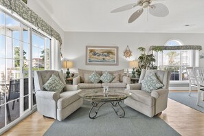 A living room with two armchairs, a glass coffee table, a sofa, and a ceiling fan. - Magnolia Place 4669-104 (Myrtle Beach)