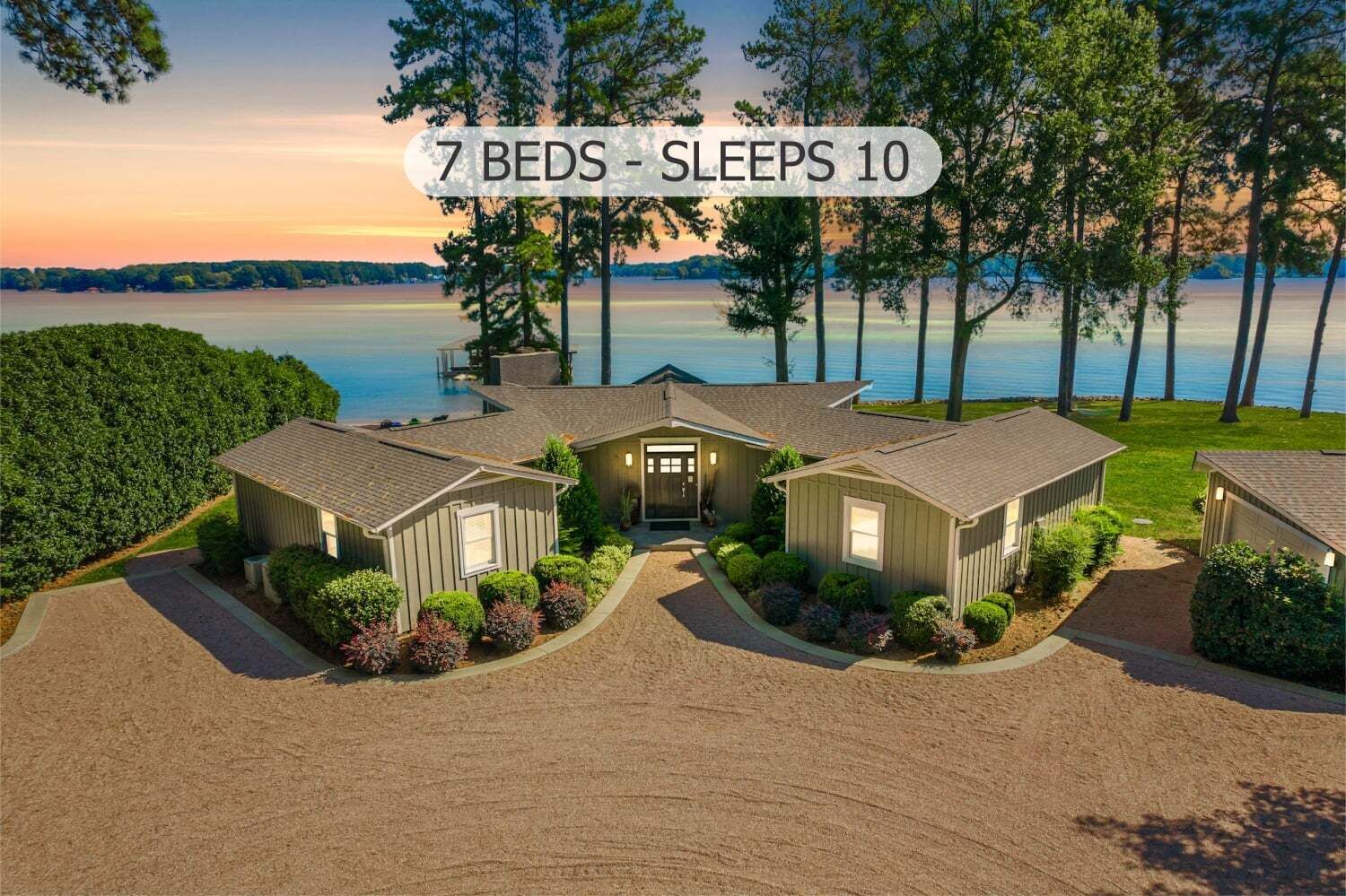 Ett hus med flera våningar, en uppfart som leder till ett garage, omgivet av välskött trädgård och med utsikt över en sjö.