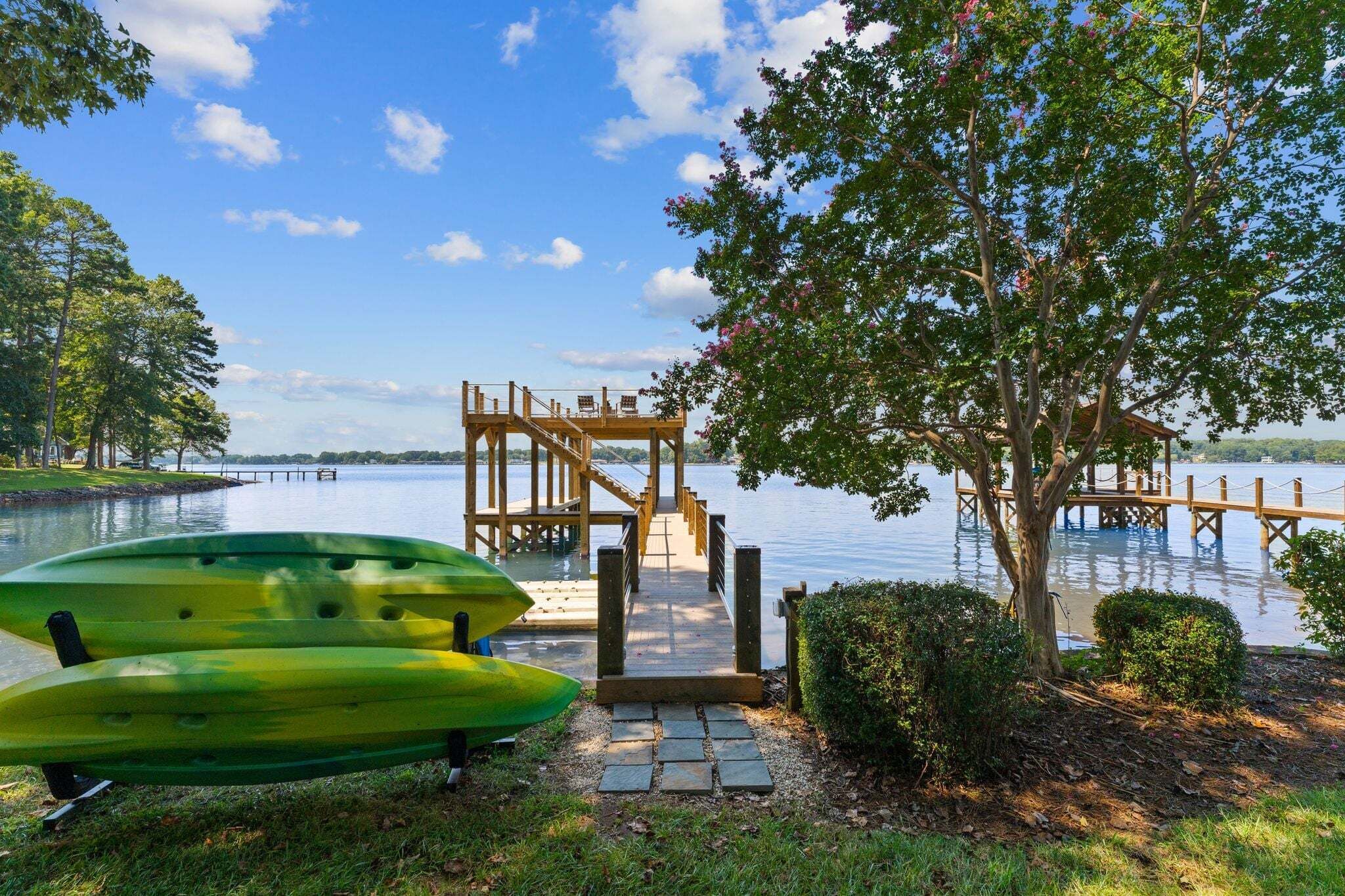 A wooden dock leading to a lake with kayaks and benches.