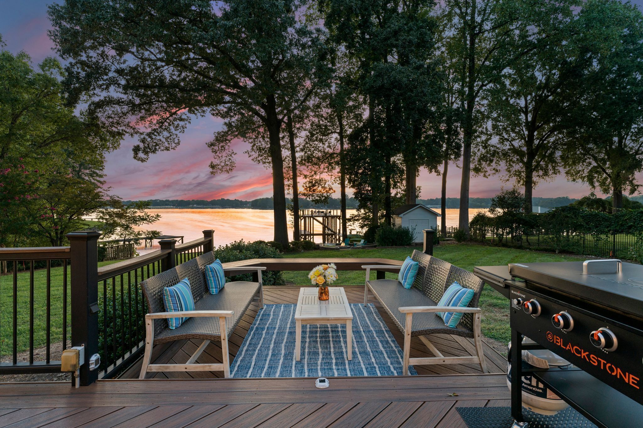 Una terraza con mobiliario exterior, una parrilla y vistas a un lago al atardecer.