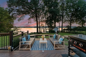 A deck with outdoor furniture, a grill, and a view of a lake at sunset. - Lakefront Living (Mooresville)
