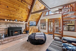 A cozy cabin interior with a fireplace, a comfortable seating area, and a spiral staircase.