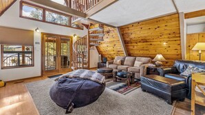 Un salon spacieux avec un grand escalier en bois, un coin salon confortable et une vue sur l’extérieur.