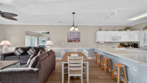 A modern kitchen with white cabinets, a central island with stools, and a dining area with a wooden table and chairs. - Magnolia North 4881-204 (Myrtle Beach)
