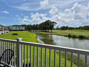 A view of a golf course with a pond, surrounded by well-maintained lawns and trees. - Magnolia North 4881-204 (Myrtle Beach)