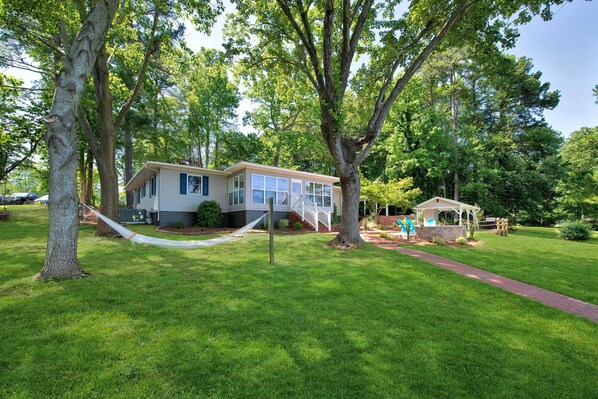 Une maison à deux étages avec un porche à l’avant, entourée d’arbres verdoyants et agrémentée d’un hamac.