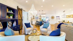 Ein geräumiges Wohnzimmer mit einer Chandelier, zwei Sofas mit blauen Kissen, einem Couchtisch und einer Küche im Hintergrund.