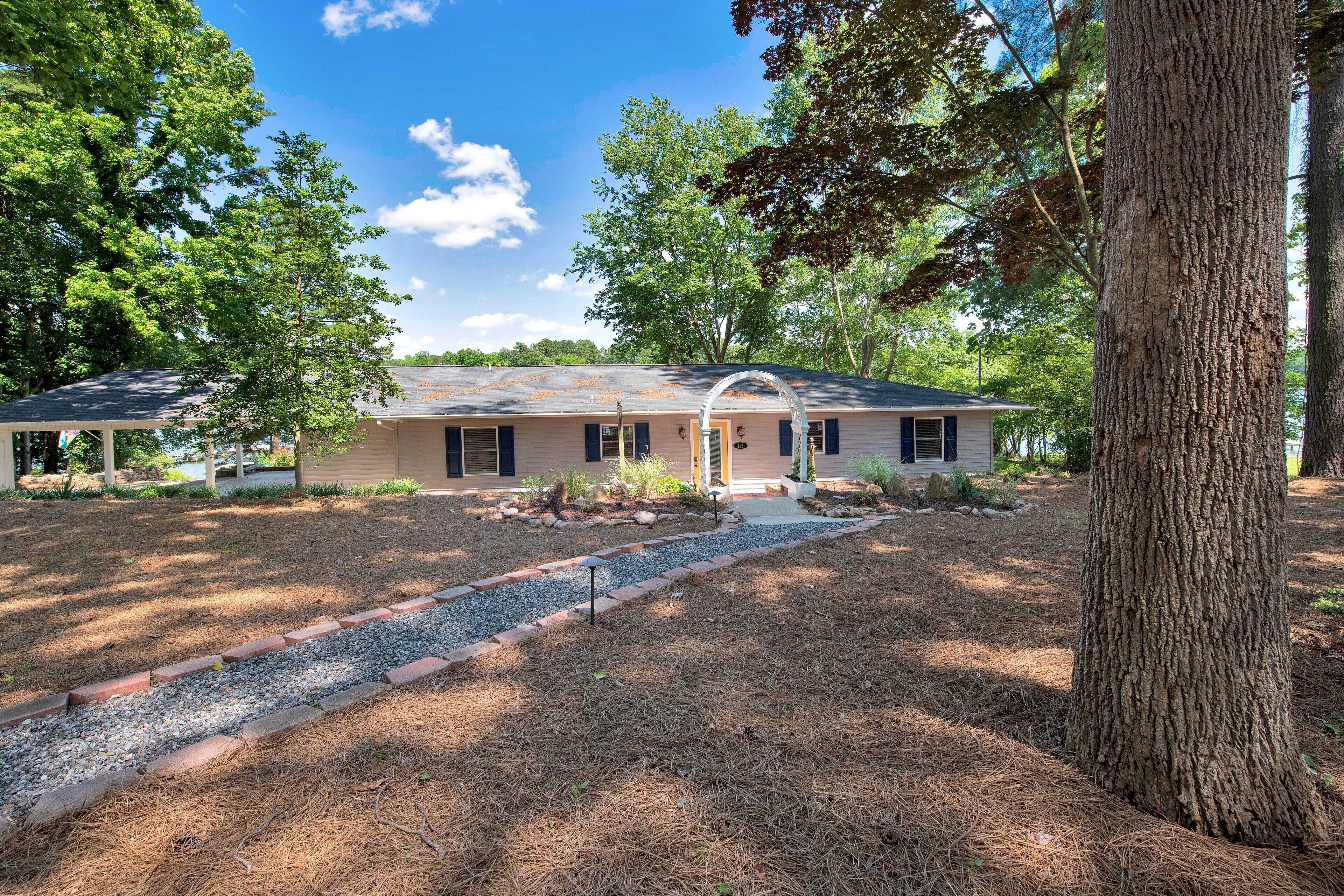 A single-story house with a front porch, surrounded by trees and a gravel pathway.