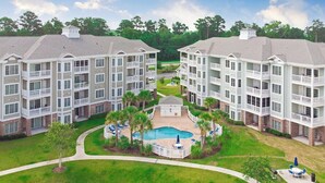A multi-story hotel with a central courtyard featuring a swimming pool, surrounded by lounge chairs and palm trees. - Magnolia Pointe Luster Leaf 4837-302 (Myrtle Beach)