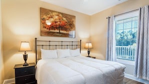 A bedroom with a large bed, two bedside tables with lamps, a window with curtains, and a painting on the wall. - Magnolia Pointe Luster Leaf 4837-302 (Myrtle Beach)