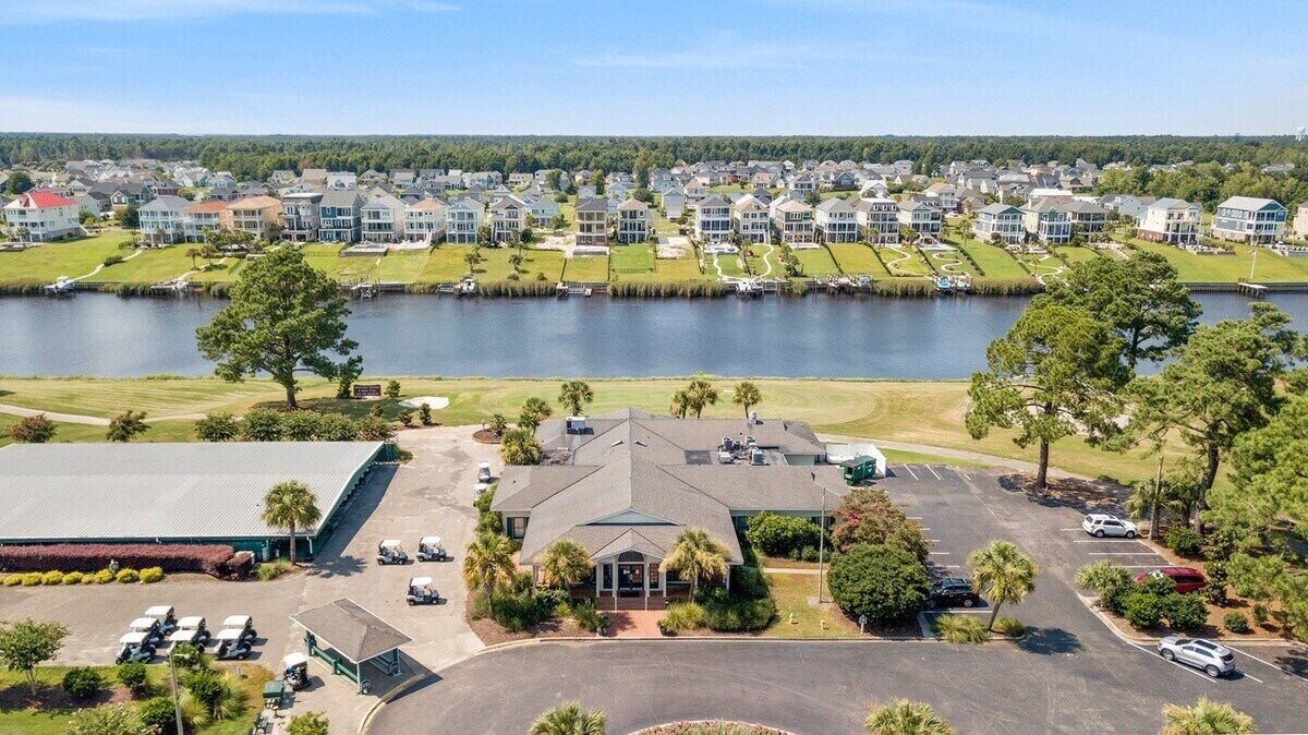 A residential area with a large building in the foreground, a parking lot, and a lake in the background.