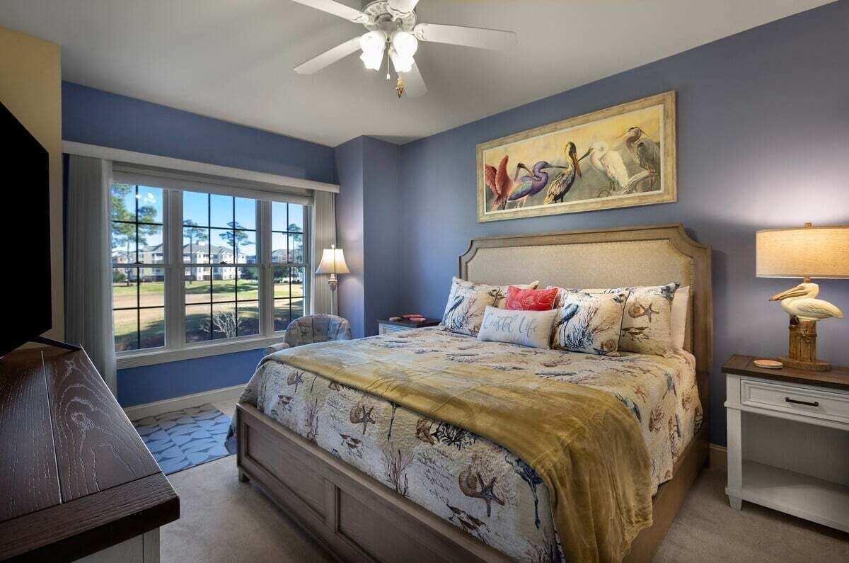 Un dormitorio con una cama grande, un ventilador de techo, una ventana con vistas a un campo de golf y un cuadro sobre la cama.