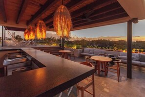 Un área de estar al aire libre con barra, mobiliario de madera y luces colgantes.