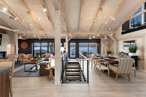 A spacious interior with a high ceiling, wooden beams, a central staircase, and large windows offering views of the outdoors. - Keenan Beach (Mooresville)