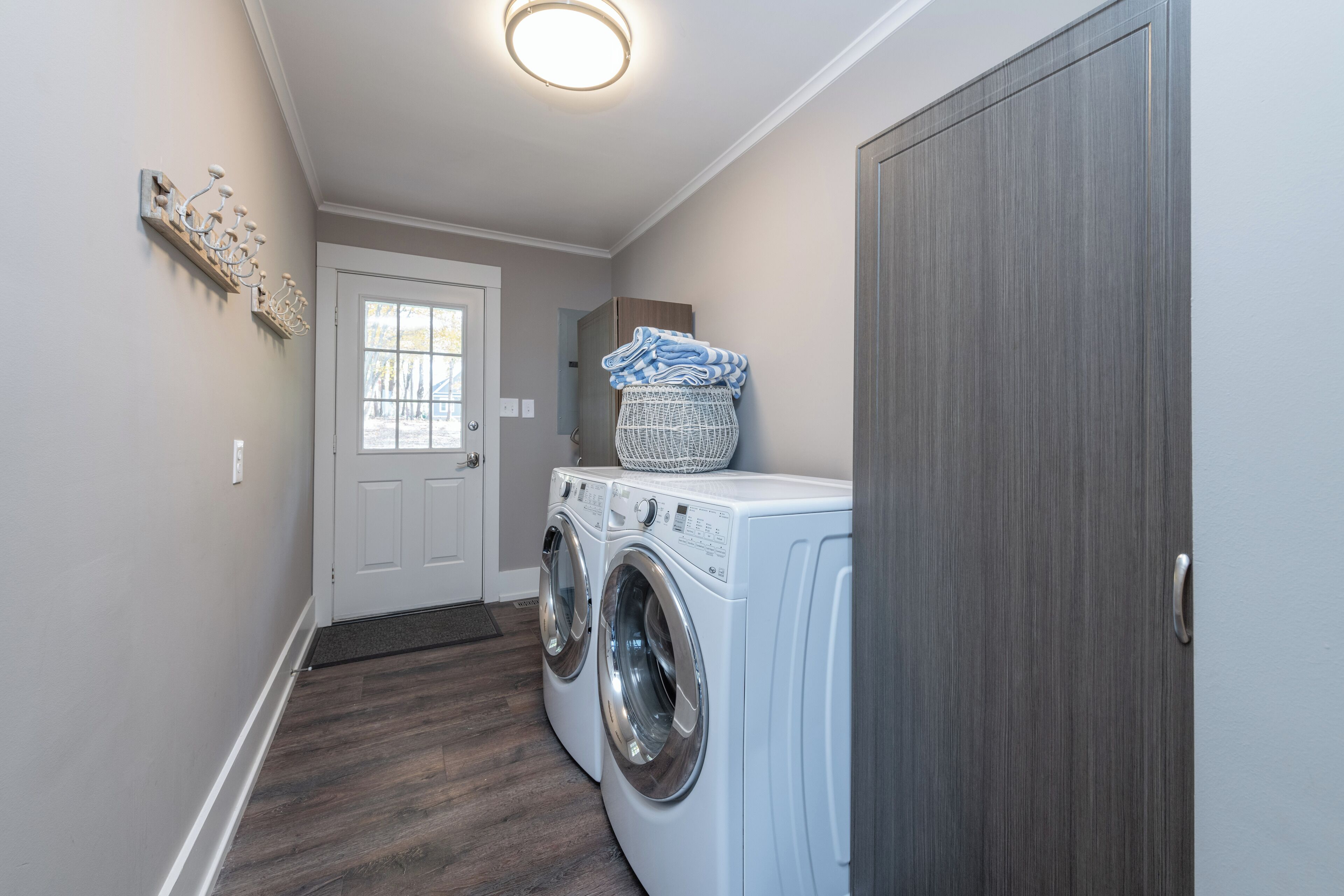 A laundry room with two front-loading washing machines, a basket on top of one, and a door leading to another room.
