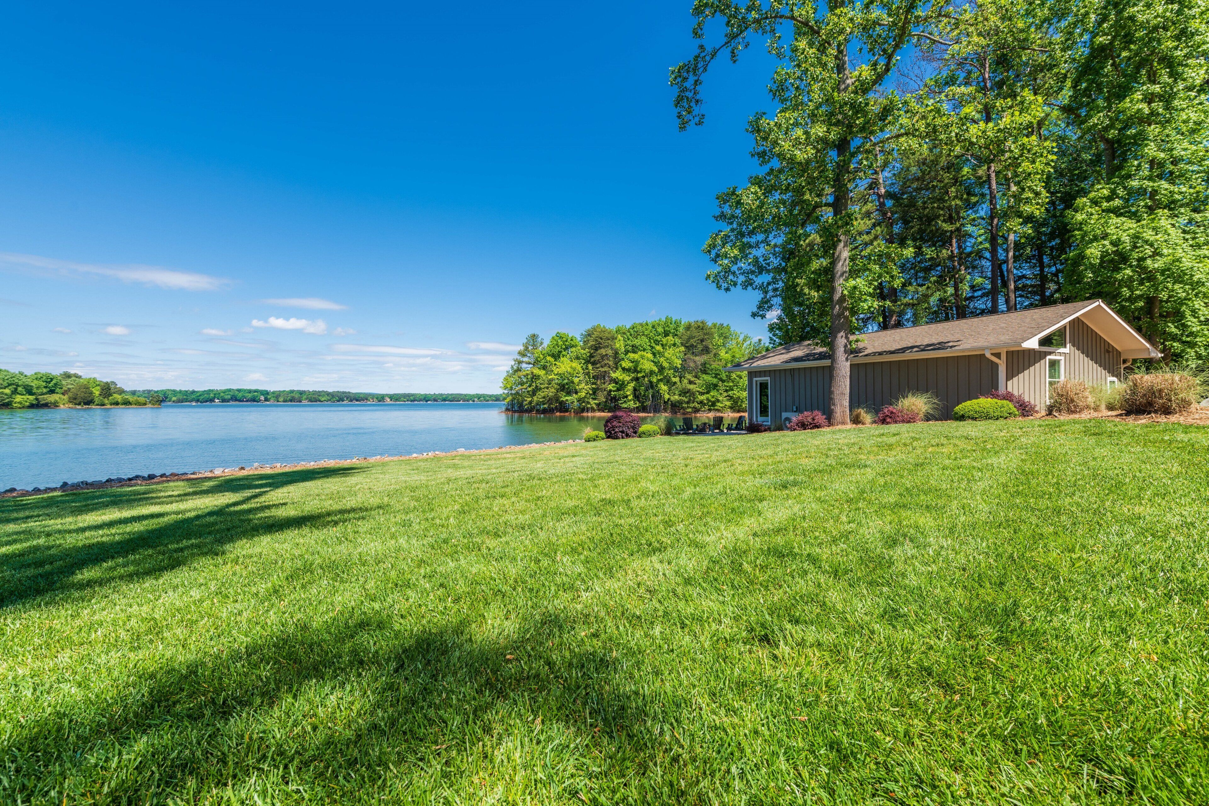 A lakeside property with a grassy lawn, a wooden cabin, and a dock extending into the water.