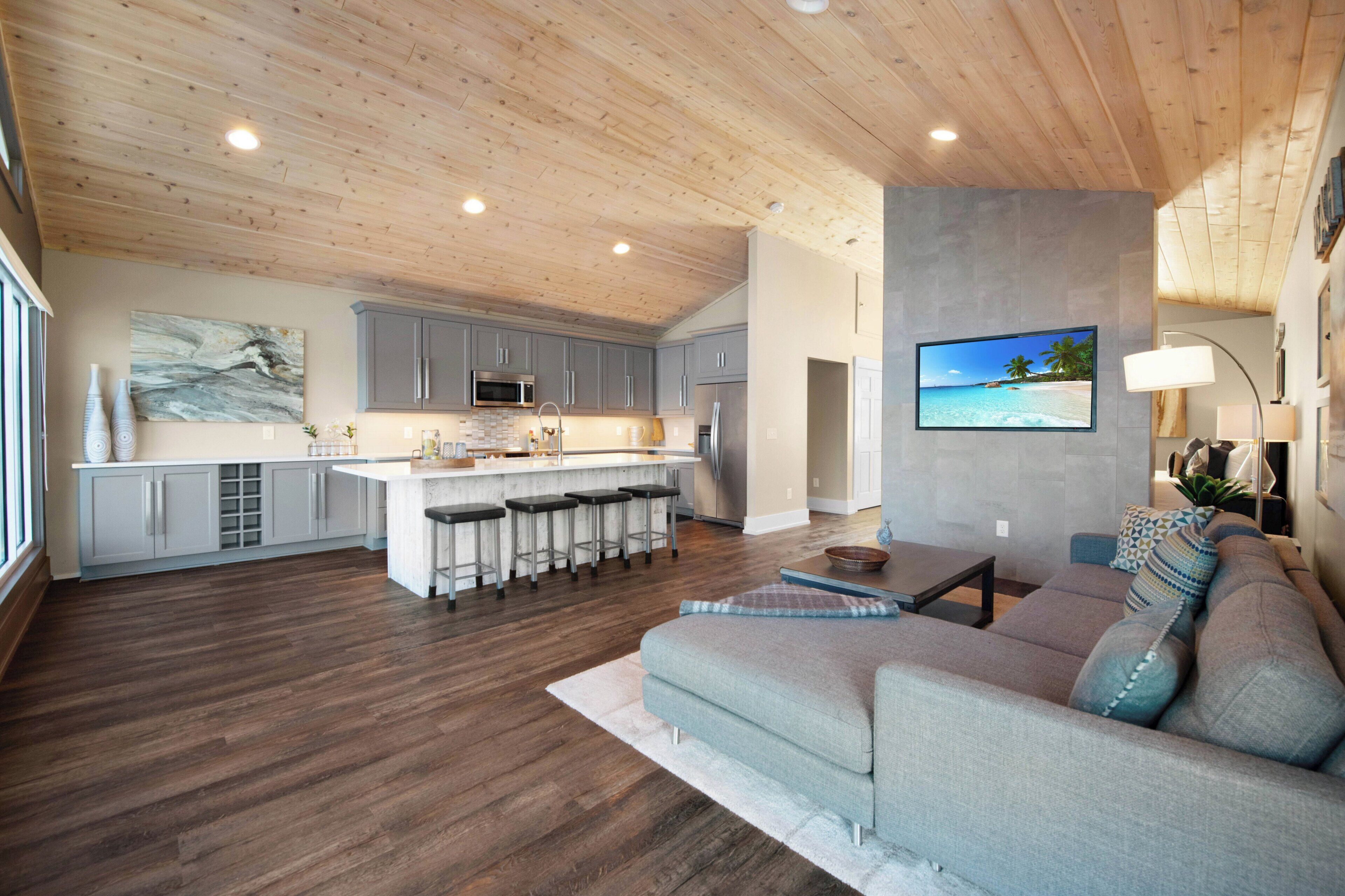 A spacious living area with a large gray sofa, wooden flooring, and a kitchen with gray cabinets and a central island.