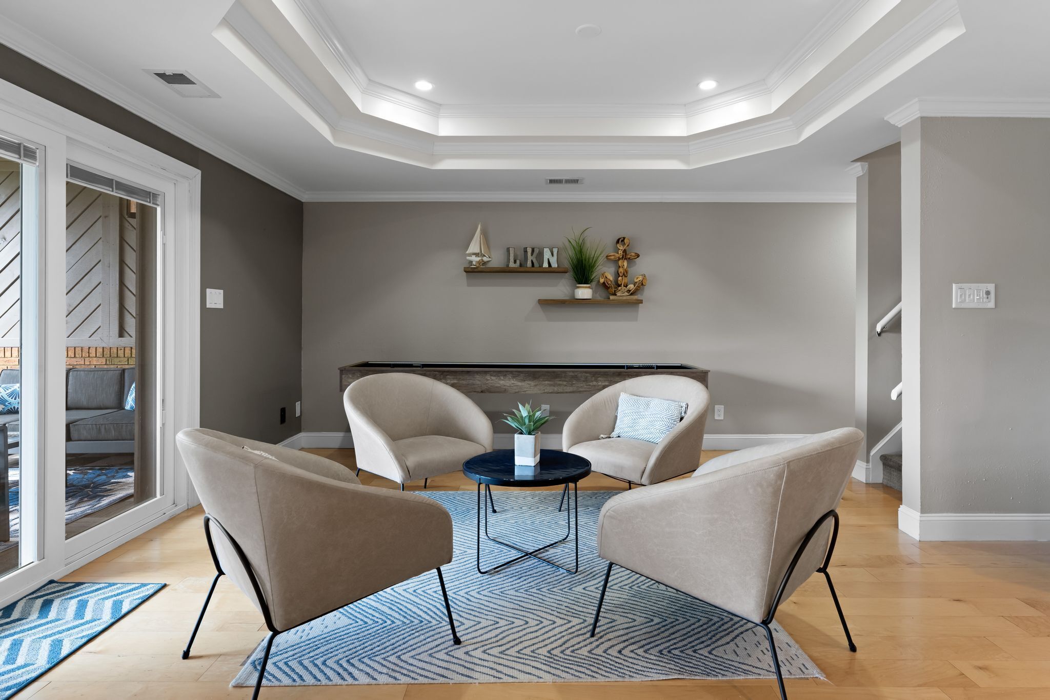 A modern living room with two beige armchairs, a small round table, and a decorative wall shelf with a plant and a small statue.