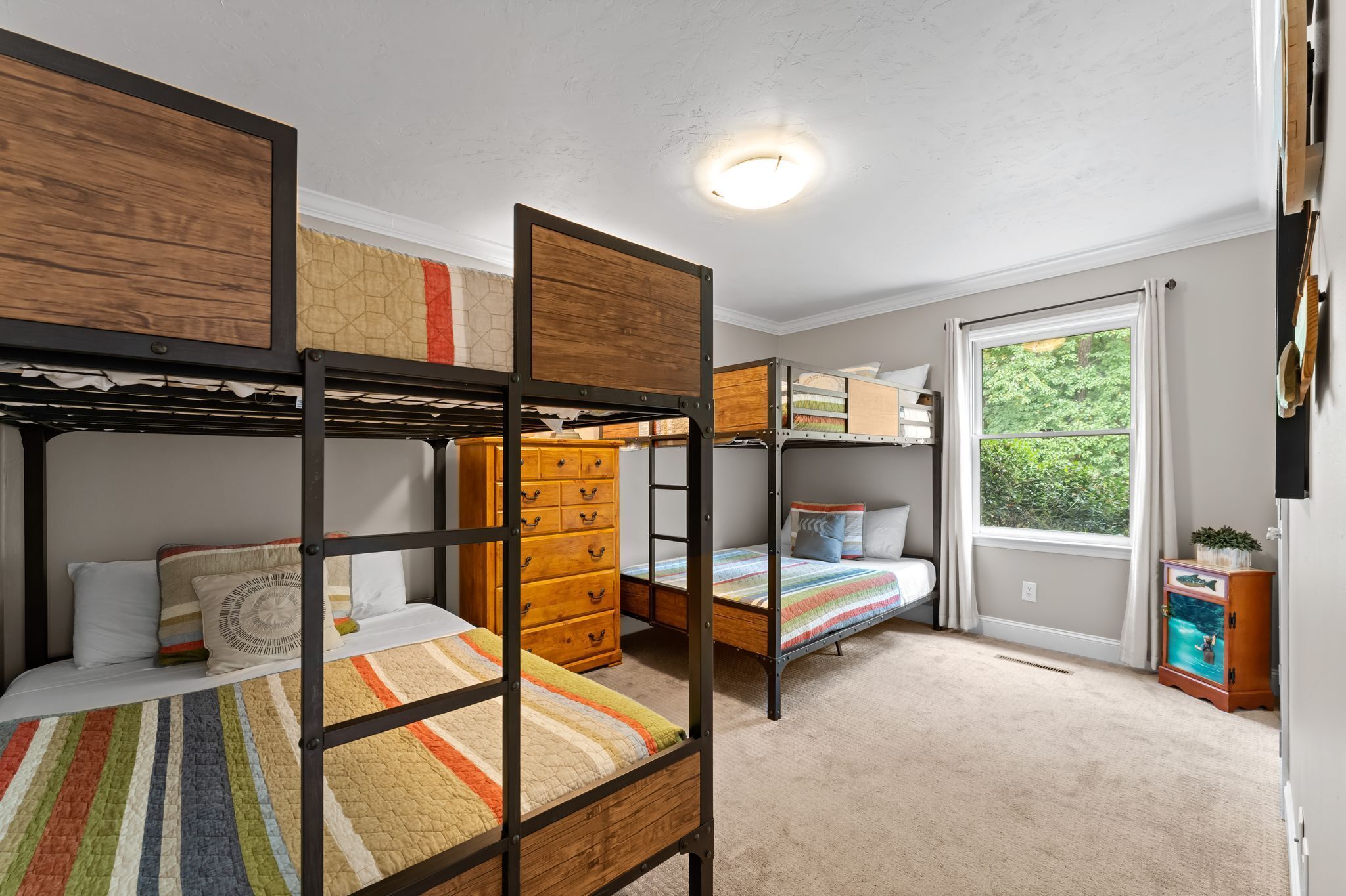 Quarto com beliche, cômoda, janela com vista para área verde e luminária no teto.
