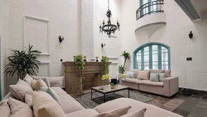 Ein geräumiges Wohnzimmer mit einer grossen Eckcouch, einem Couchtisch und einem Kamin. Es gibt einen Balkon mit Geländer und ein grosses Fenster mit blauer Umrandung.