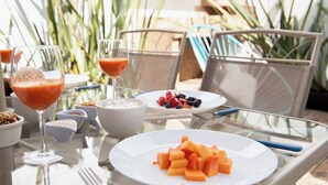 Ein Tisch ist gedeckt mit Obsttellern, einem Glas Orangensaft und einem Glas Weißwein.