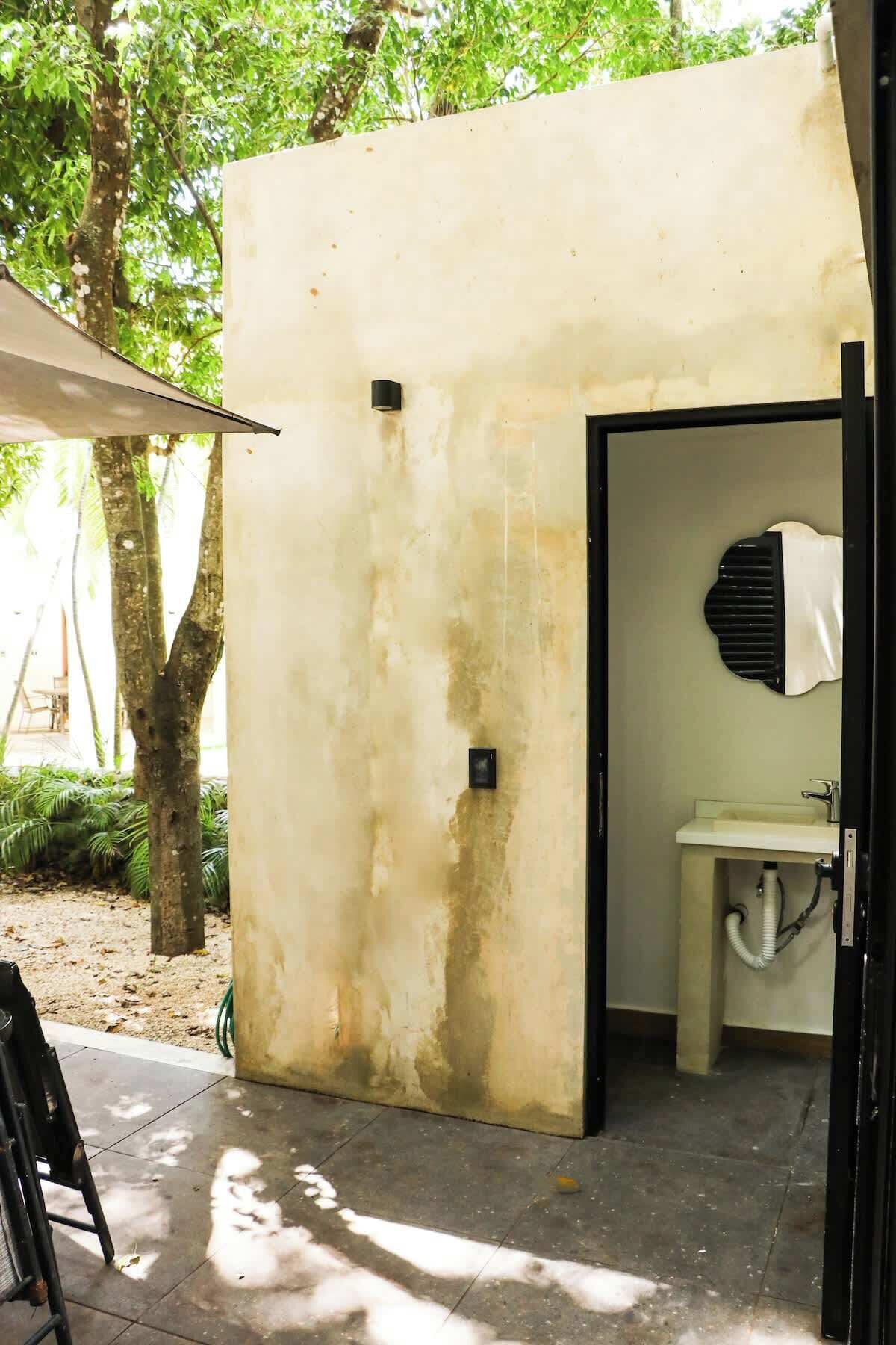 A small, single-room structure with a toilet and sink, a door, and a small window.